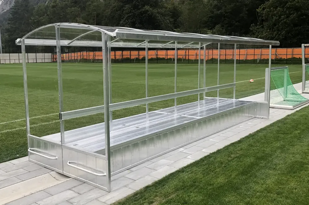 Eine doppelte Aluminium Spielerkabine mit Dach und Plexiglasscheiben auf Sportplatz