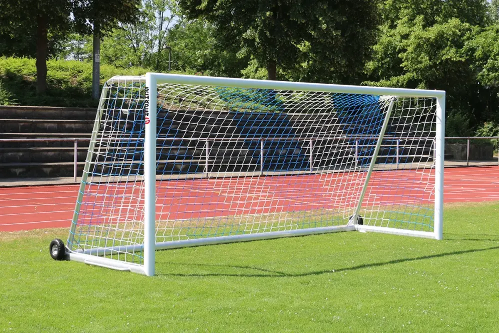 Ein weißes Fußballtor mit rot/weißen Netz und Rädern auf Fußballplatz