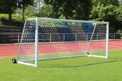 Ein weißes Fußballtor mit rot/weißen Netz und Rädern auf Fußballplatz