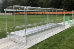 Eine doppelte Aluminium Spielerkabine mit Dach und Plexiglasscheiben auf Sportplatz